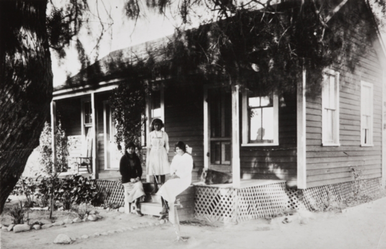Sally Ortega, standing, and Vera Ortega, on viewer's right, with school friend, at viewer's left, at their home in San Fernando ; the silhouette in the window is of Isidora Ortega, mother of Sally and Vera.